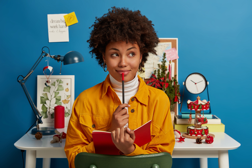 Woman sitting at desk, holding a pencil and thinking.